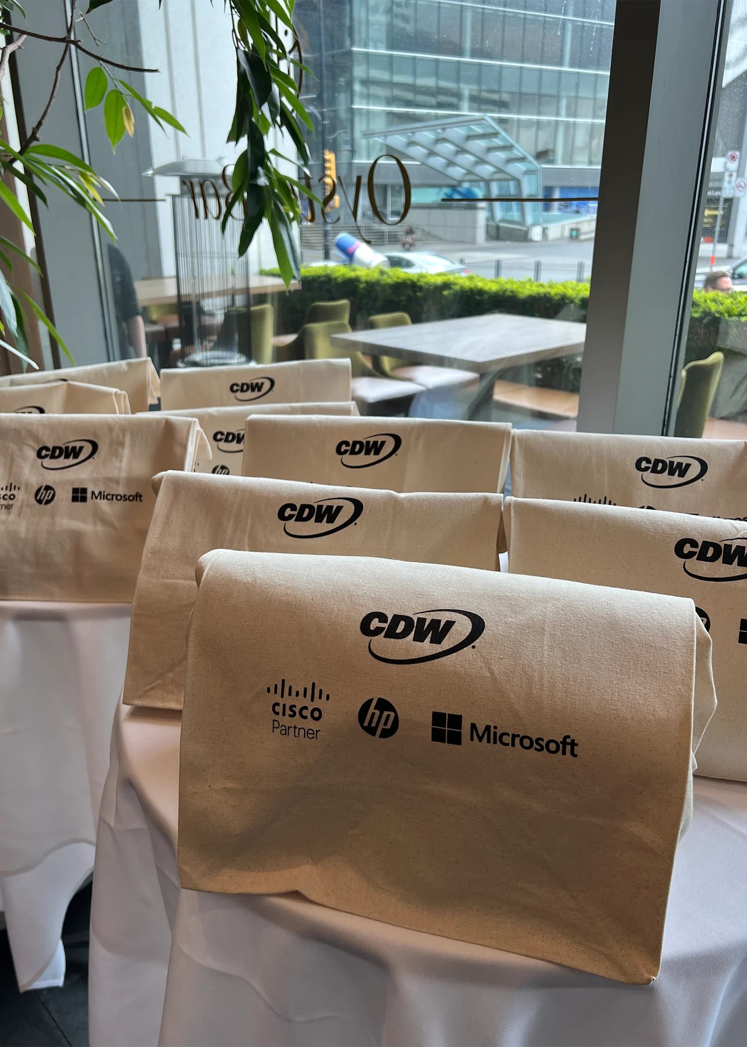 Rows of kraft paper gift bags branded with the CDW, Cisco, HP, and Microsoft logos set out on tables