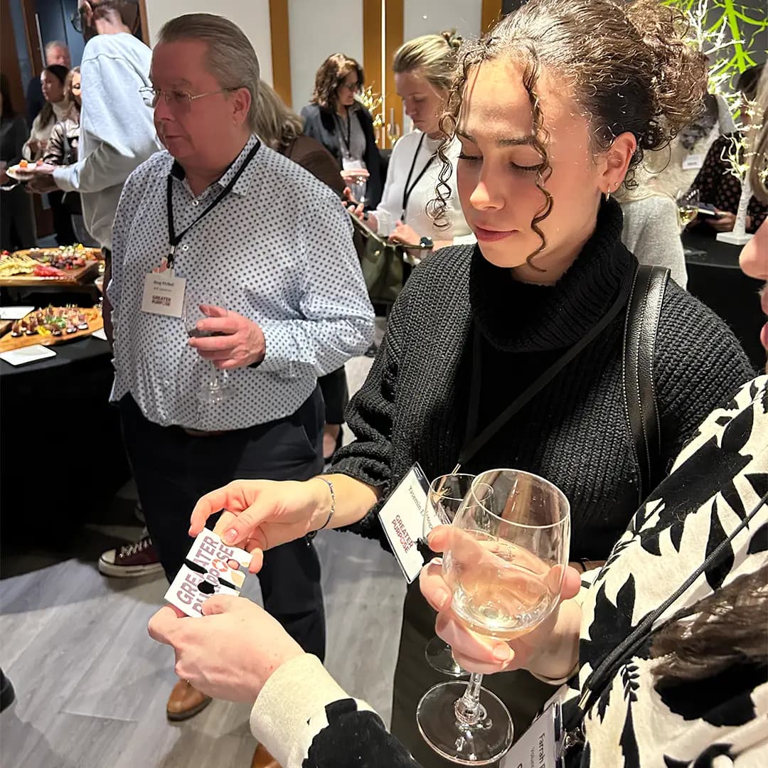 Attendees mingling at a Greater Purpose networking event, comparing their puzzle-piece cards while holding wine