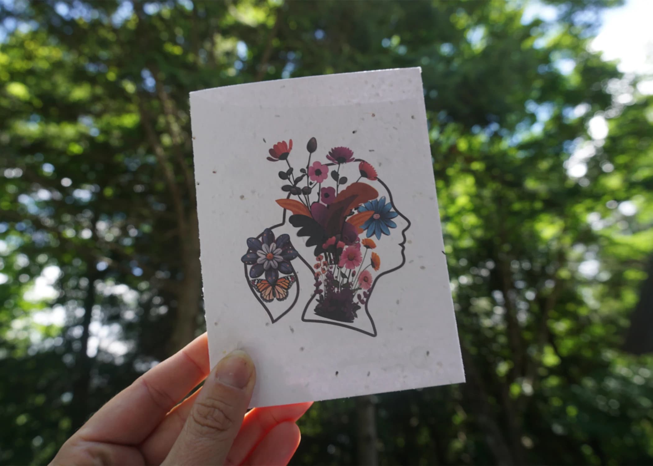 Hand holding a Jane Goodall Institute Canada plantable seed paper card printed with a floral silhouette design