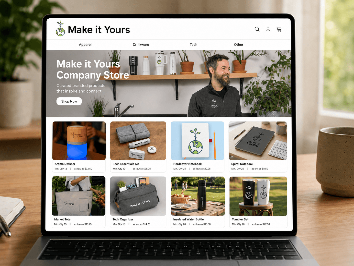 Laptop displaying a branded online company store website with a hero banner and a grid of branded products including drinkware, notebooks, and bags, each listed with minimum order quantity and price
