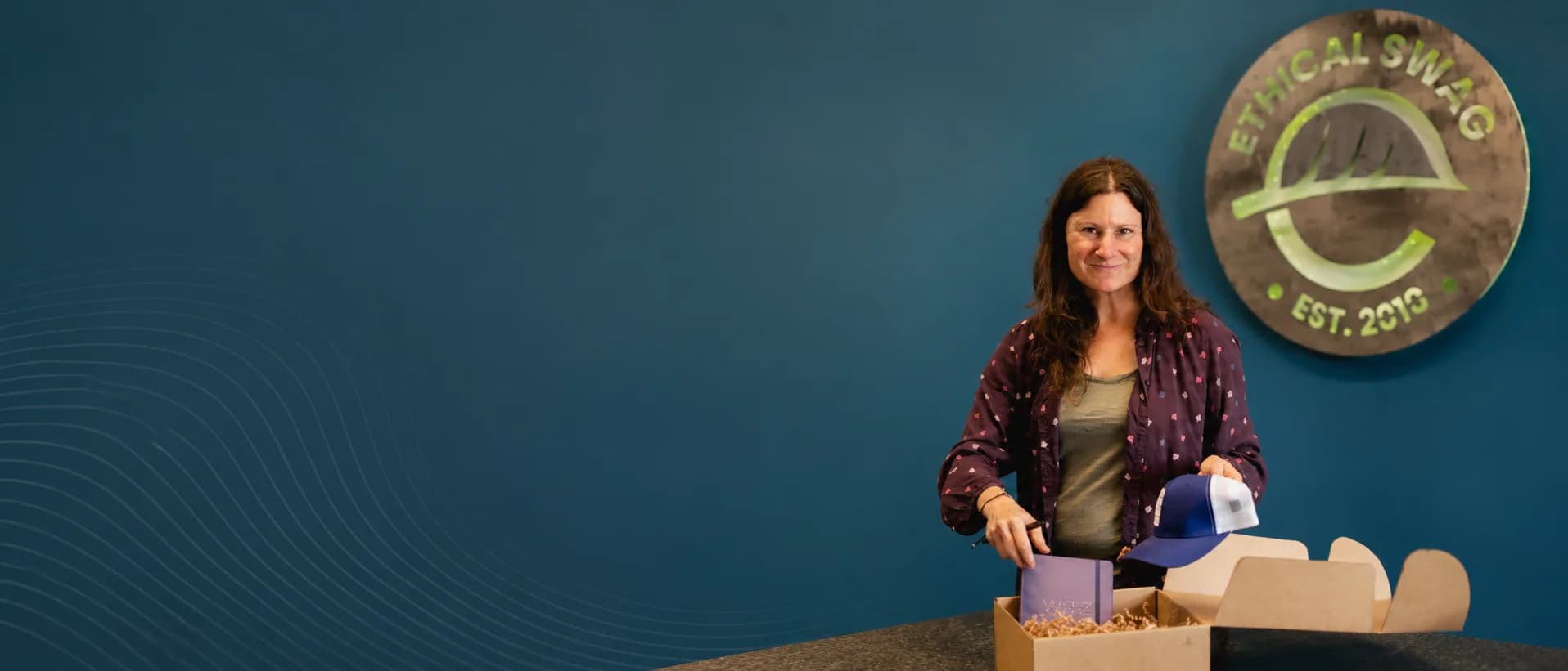 Ethical Swag team member packing a branded cap and notebook into a kraft gift box at the warehouse