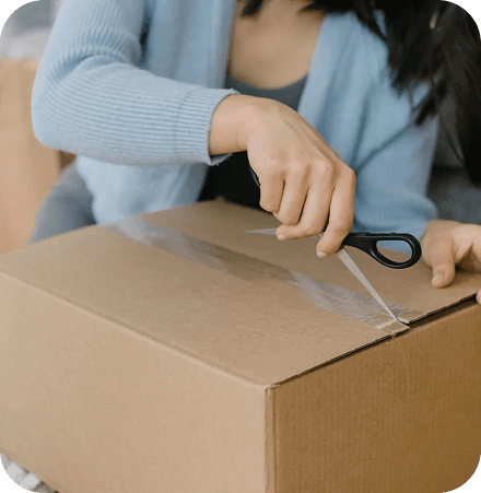 Hands carefully sealing a brown cardboard box with clear packing tape, indicating meticulous and stress-free packaging.