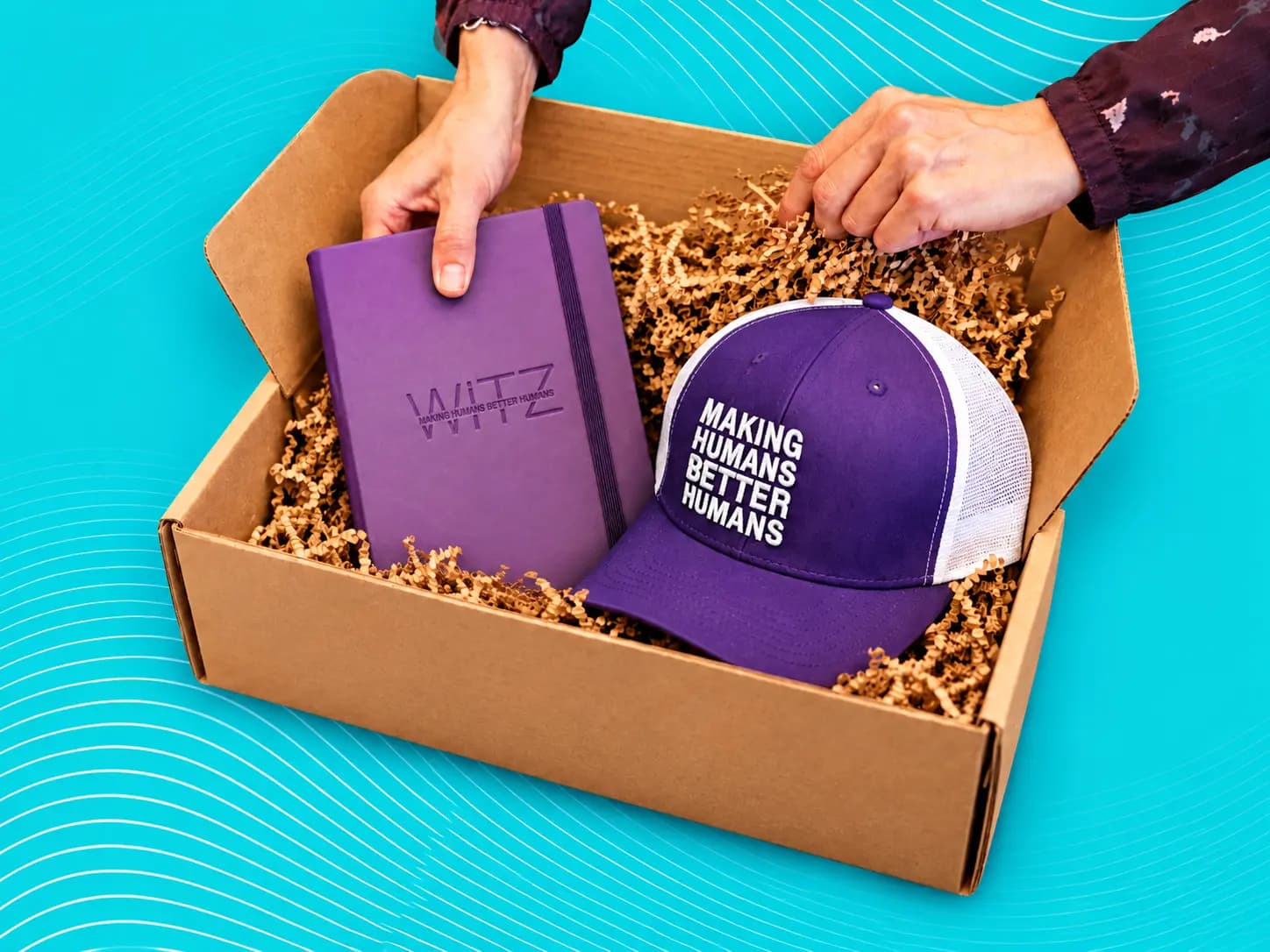 Hands placing a purple notebook and cap into a Swag Pack box