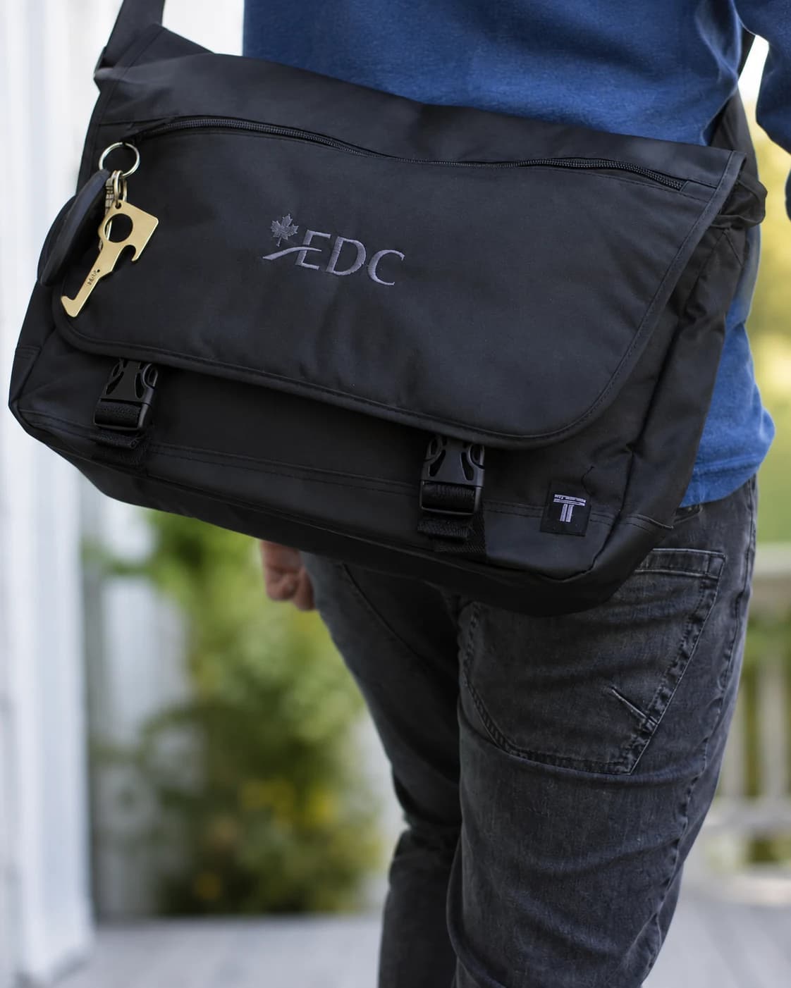 New hire wearing an EDC-branded messenger bag with a brass no-touch door-opener key attached