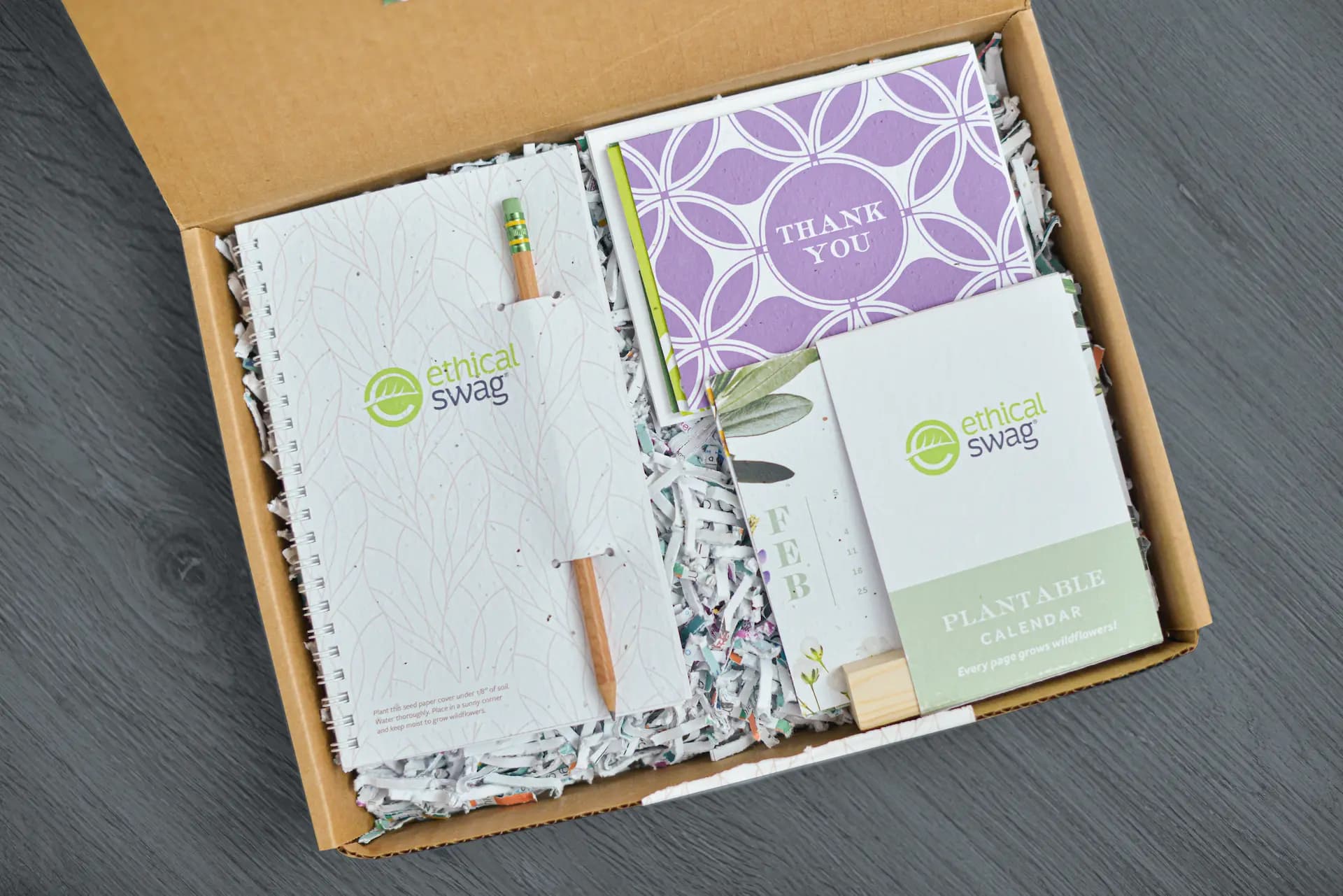 Open branded swag pack box with notebook, thank you card, plantable calendar and Ethical Swag merchandise