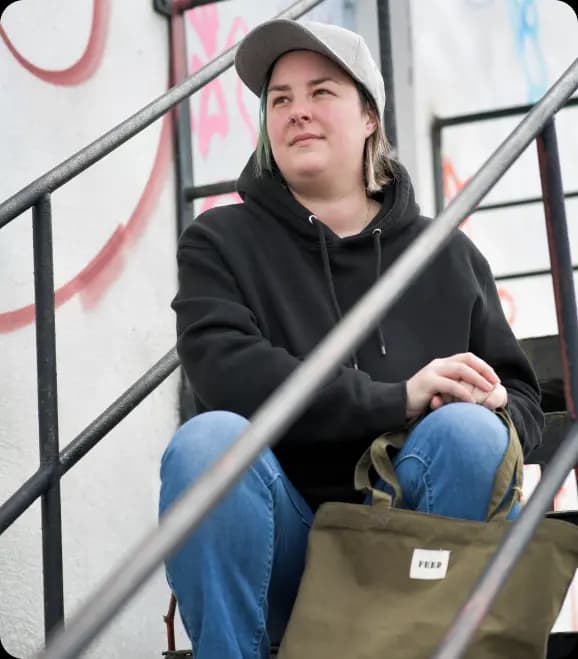 Person sitting on metal stairs holding an olive green tote bag in a casual setting