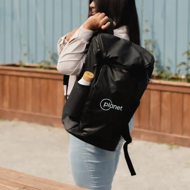 Person carrying a black backpack with a water bottle in the side pocket, outdoors